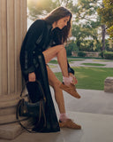 Woman in a black dress and brown shoes standing outdoors with a green handbag.
