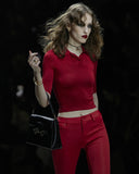 Woman in a red outfit holding a black handbag against a dark background